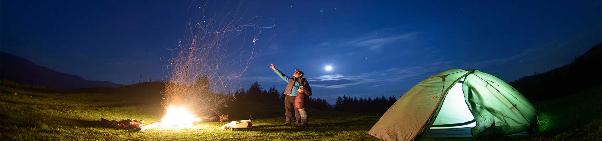 Dad and child enjoying the night sky with fire and tent in foreground