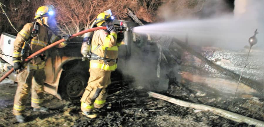 Two firemen holding hose spraying towards fire