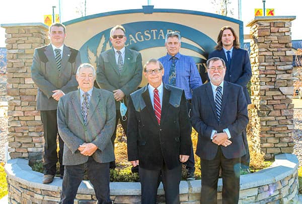 Seven men in suits standing in front of large sign